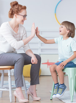 Eine junge roothaarige Therapeuten klatscht mit einem kleinem Jungen ab. Beide freuen sich über die Erfolge in der Therapie.