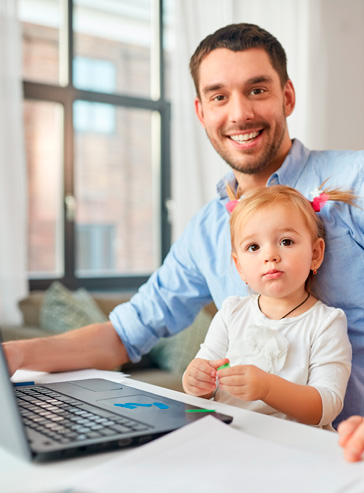 Ein junger Familienvater sitzt zu Hause mit seiner kleinen blondhaarigen Tochter auf dem Schoß vor einem Laptop