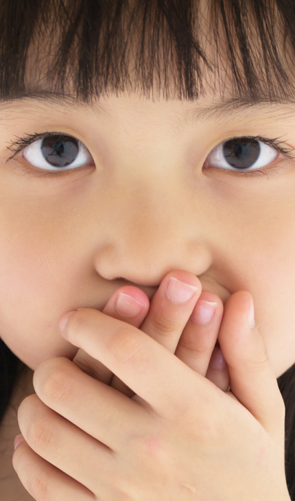 Kleines Mädchen mit dunklen Haaren hält beide Hände vor den Mund