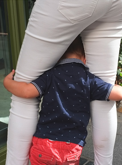 Ein kleiner Junge hält sich zwischen den Beinen seiner Mutter fest