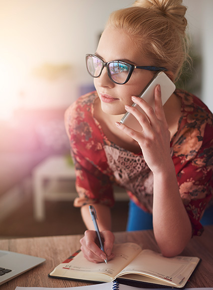 Eine junge Frau telefoniert mit einem Handy und macht sich in ihrem Kalender Notizen