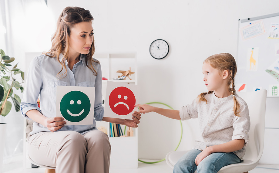 Psychologin zeigt kleinem Kind glückliche und traurige Gefühle