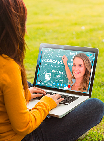 Eine Frau sitzt mit einem Laptop auf einer Wiese und nimmt an einem Seminar teil