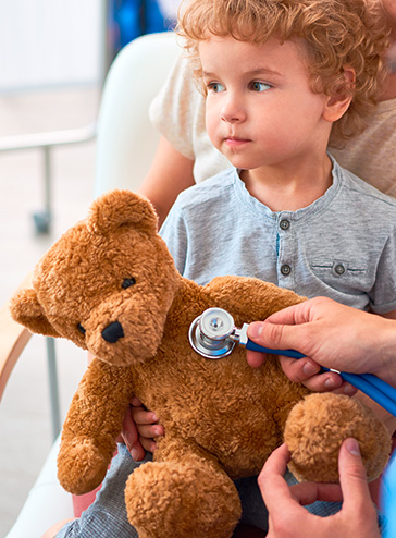 Kleiner Junge mit Teddybären auf dem Schoß, der untersucht wird