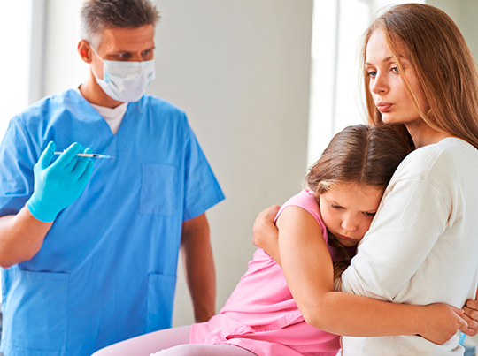 Ein kleines Mädchen hat Angst vor einer Spritze und klammert sich an ihrer Mutter fest