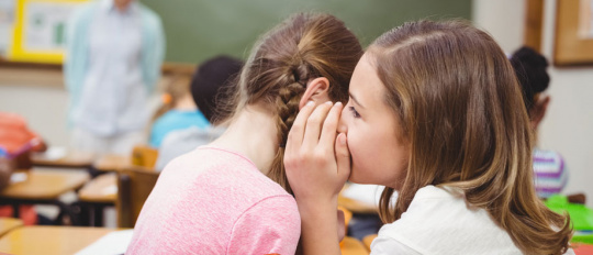 Während des Unterrichts flüstert ein Mädchen ihrer Nachbarin etwas ins Ohr