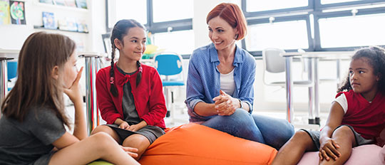 Ein Gruppe von Kindern sitzt gemeinsam mit einer Therapeutin im Halbkreis auf Sitzkissen